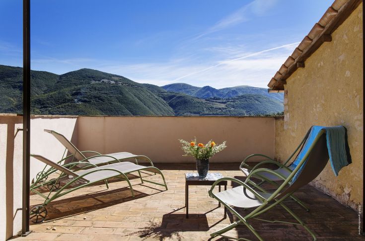 An outdoor terrace with sun loungers, overlooking a mountain panorama.