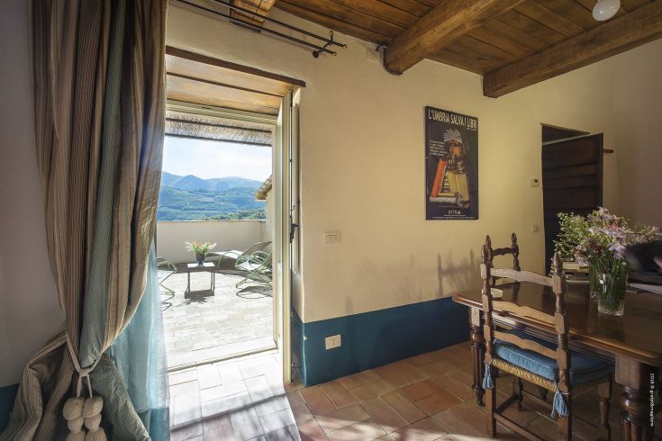 Interior of a historic building in Postignano, featuring access to a terrace with a view of the surrounding landscape.