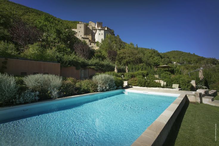 A scenic view of Postignano Castle surrounded by nature, featuring a visible swimming pool.