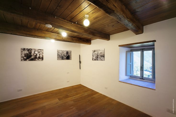Interior of a palace with light walls, wooden beams, and photographs, softly illuminated by lamps.