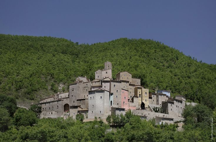 The medieval village of Postignano is located on a hill, surrounded by greenery and historical features.