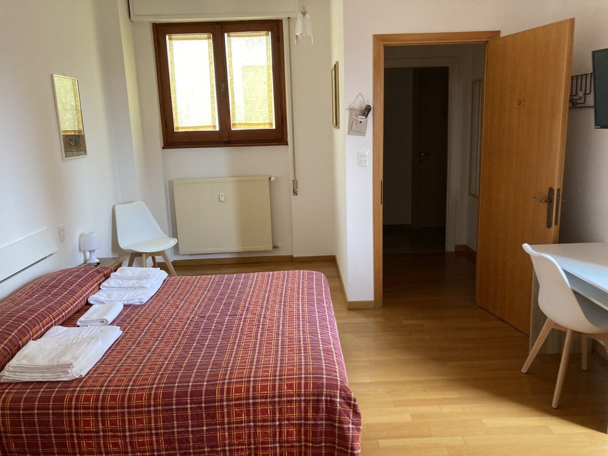 Camera confortevole con letto matrimoniale e arredi semplici. Illuminata da finestre ampie.