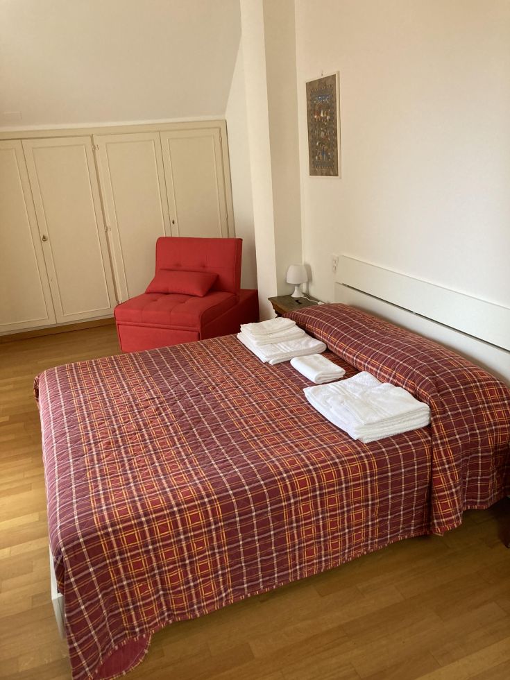 Geräumiges und gut beleuchtetes Zimmer mit einem Doppelbett und einem roten Sofa, ordentlich und bequem.