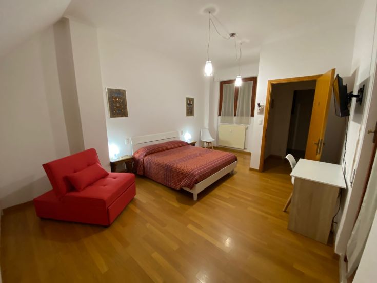 Geräumiges und helles Zimmer mit einem Doppelbett, Sofa, TV und einfacher Einrichtung.