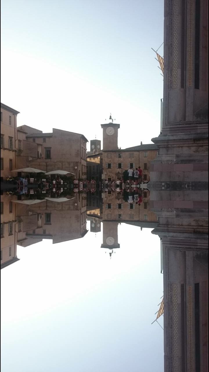 Una scena di una piazza in una città umbra, con un orologio che segna l'ora.