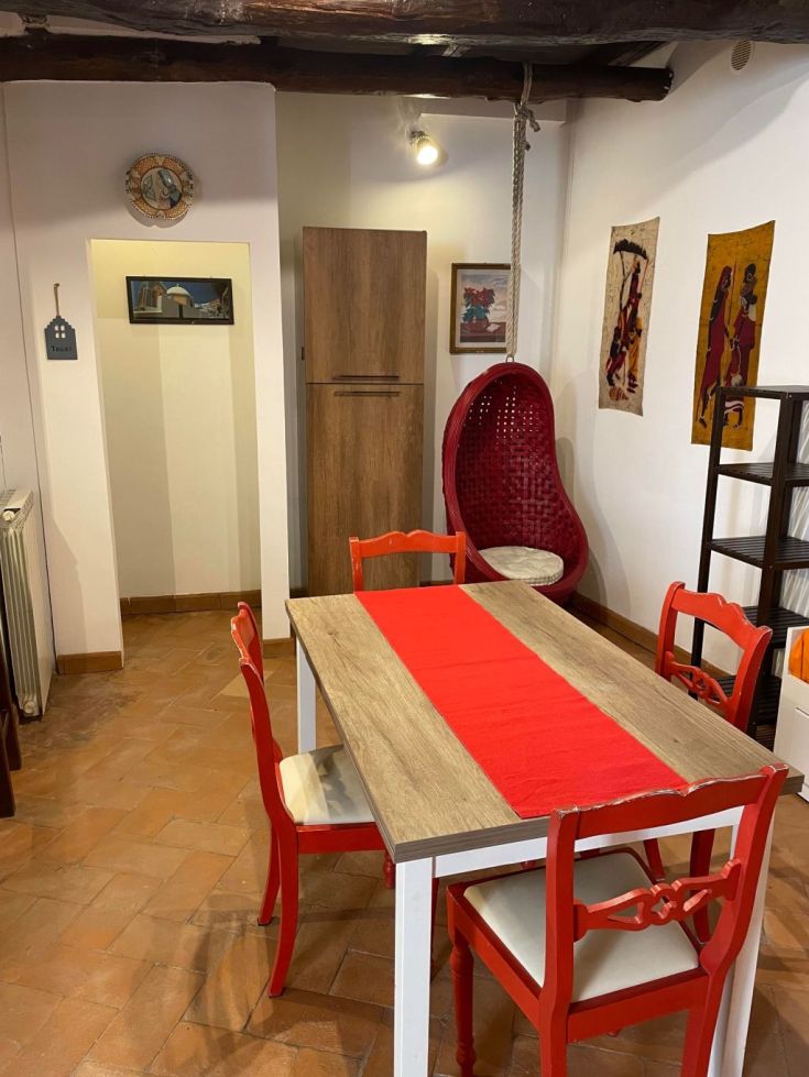 Una sala da pranzo semplice con mobili in legno e lampade; i dettagli rossi aggiungono un tocco di colore.