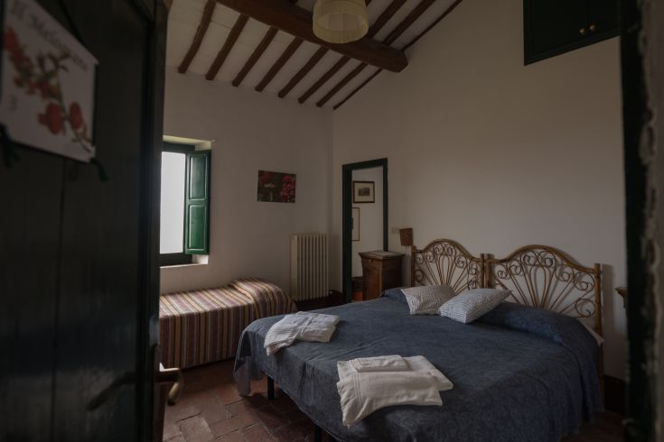 Camera confortevole in agriturismo con letto matrimoniale e letto singolo. Una finestra verde offre luce naturale.