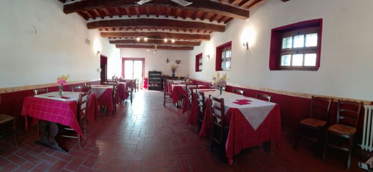 Spazio interno con tavoli di legno e sedie in un agriturismo in Umbria, con tonalità calde e arredamento semplice.