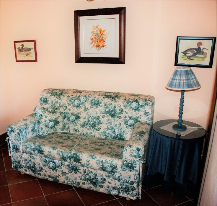 Accogliente salotto con divano decorato e lampada, circondato da elementi decorativi in un'atmosfera familiare.