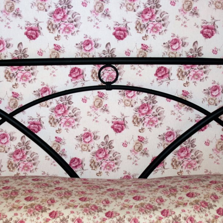 Particolare di un letto con testiera nera e un rivestimento floreale in tonalità rosa.