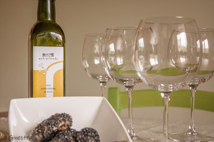 A table set with a bottle of extra virgin olive oil and wine glasses prepared for a meal.
