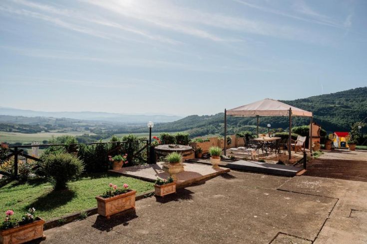 Building surrounded by greenery, featuring a gazebo and a view of the surrounding hills.