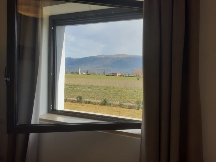 Scena di prateria e montagne osservabile da una stanza con finestra aperta.