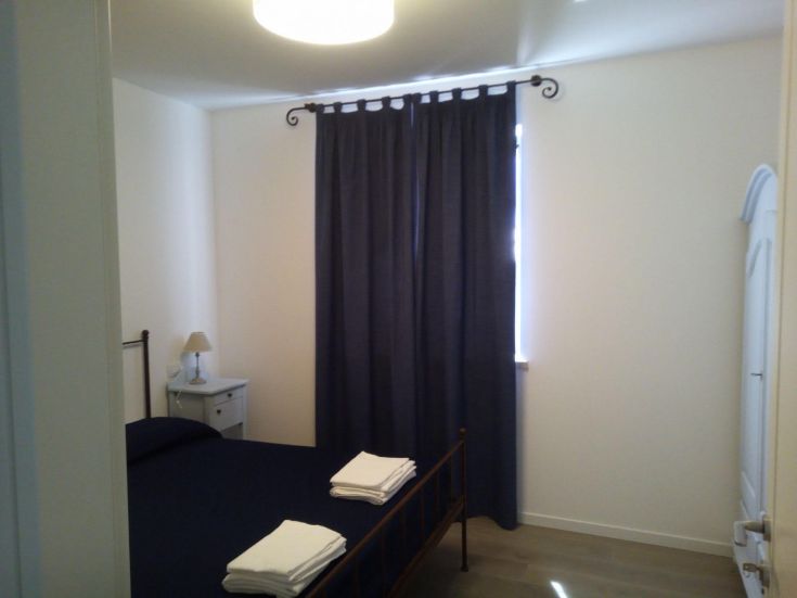 Una camera luminosa con letto matrimoniale, pouf e tende oscuranti che creano un'atmosfera confortevole.