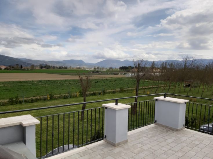 Scena tranquilla della campagna umbra, caratterizzata da campi verdi e rilievi montuosi sullo sfondo.