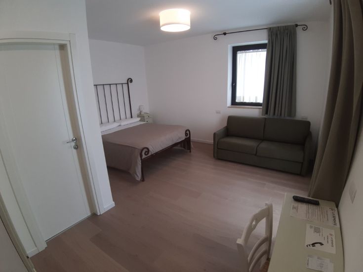 Camera accogliente dell'agriturismo, con letto matrimoniale, divano e decorazioni semplici. Spazio ben illuminato.