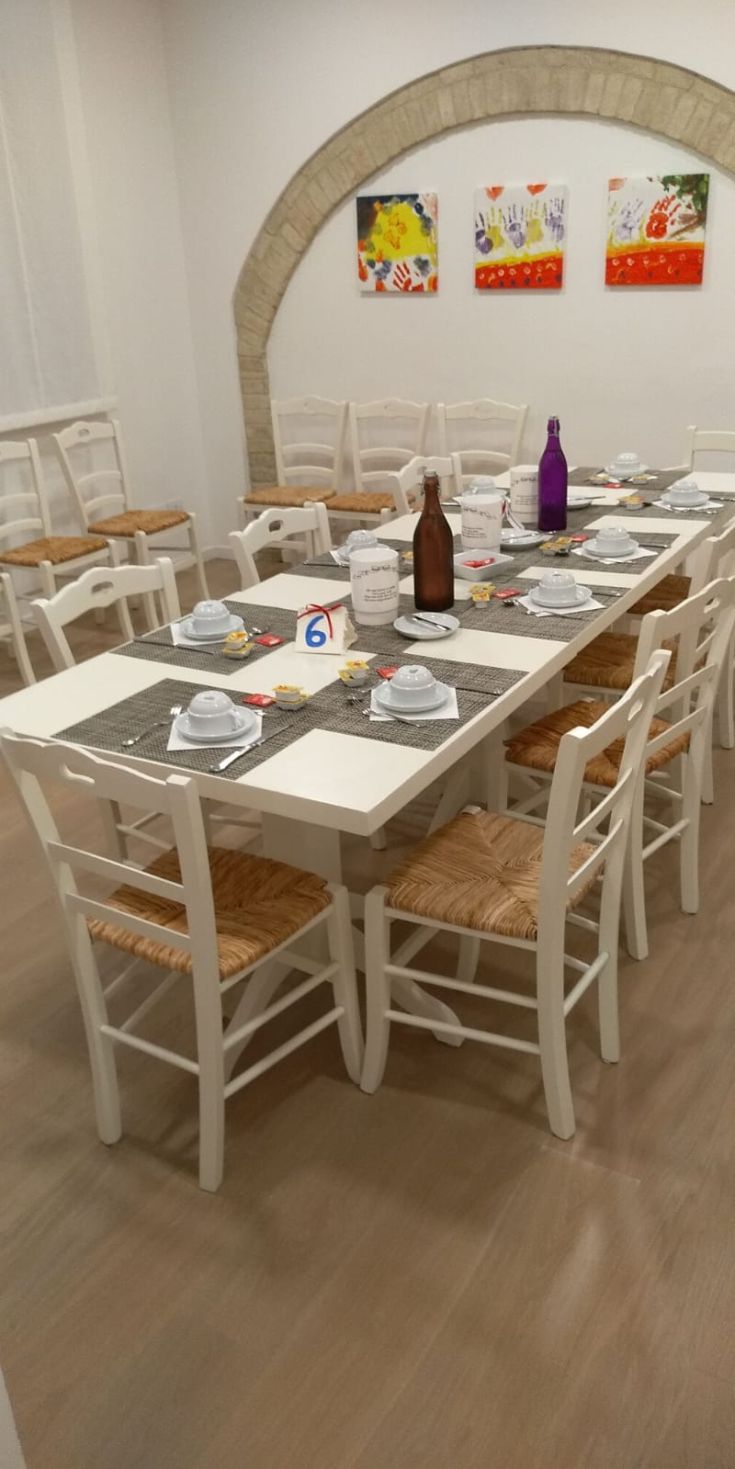 Una sala da pranzo semplice con tavoli bianchi e sedie in legno, arredata in modo sobrio.