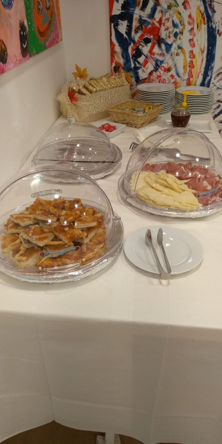 Un buffet allestito con piatti coperti da coperchi trasparenti e decorazioni sullo sfondo.