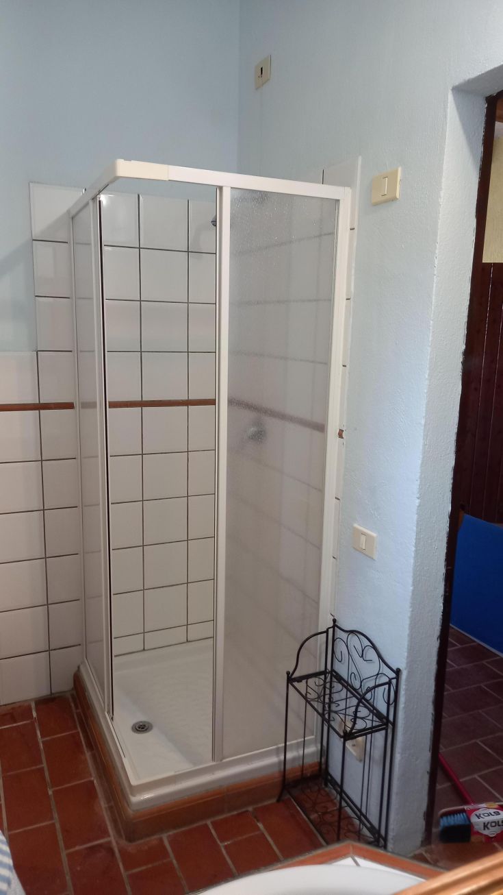 Modern shower in a bathroom with light tiles and terracotta floor, a simple and practical space.