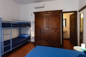 Interno di una camera caratterizzato da letti a castello e un armadio in legno. Arredamento sobrio e luminoso.