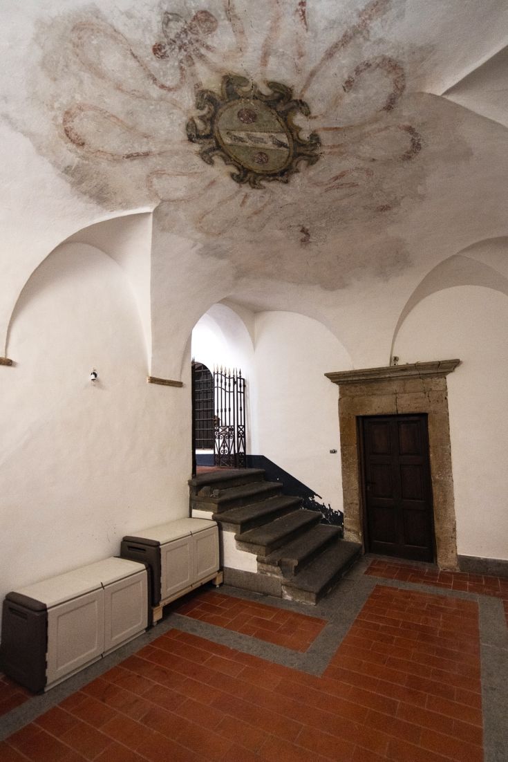 Interno di un edificio con decorazioni al soffitto e scale in pietra. Ambiente semplice e accogliente.