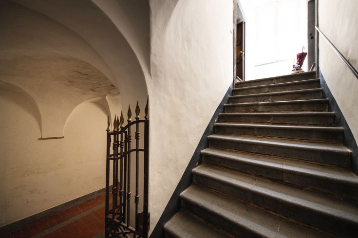 Dettaglio di una scala che conduce a una porta ben illuminata, con un cancello decorativo.