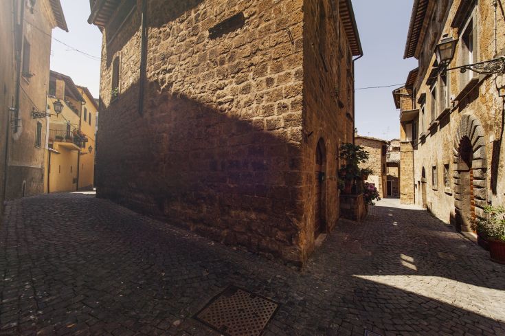 Un tranquillo vicolo di un borgo storico, caratterizzato da edifici in pietra e dettagli floreali curati.
