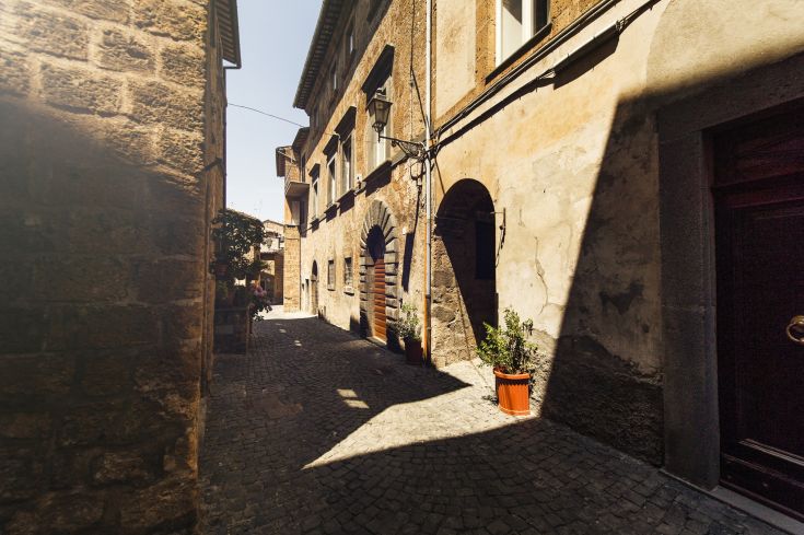 Un tranquillo vicolo con case in pietra e vasi di piante, circondato da un cielo sereno.
