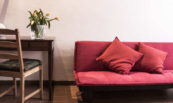 Un soggiorno semplice con un divano rosso e un tavolo in legno, decorato con fiori gialli.