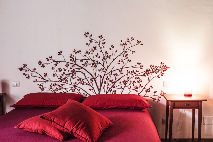 Camera semplice con decorazioni che richiamano rami e cuscini di colore rosso.