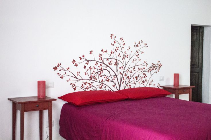 Camera da letto semplice con letti rossi e decorazioni floreali su una parete.