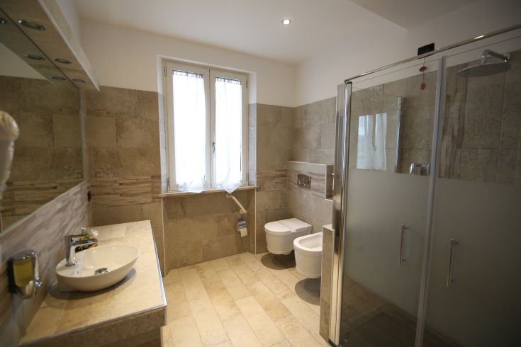 Modern bathroom with stone finishes and a spacious shower, featuring windows for natural light.