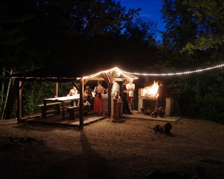 Ein ruhiger Abend im Freien mit einem brennenden Kamin und sanften Lichtern, umgeben von Tischen für Entspannung und Geselligkeit.