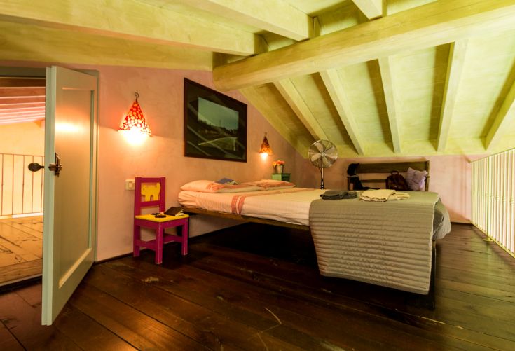 Einfaches Zimmer mit sichtbaren Balken, Doppelbett und lebhaften Farben.