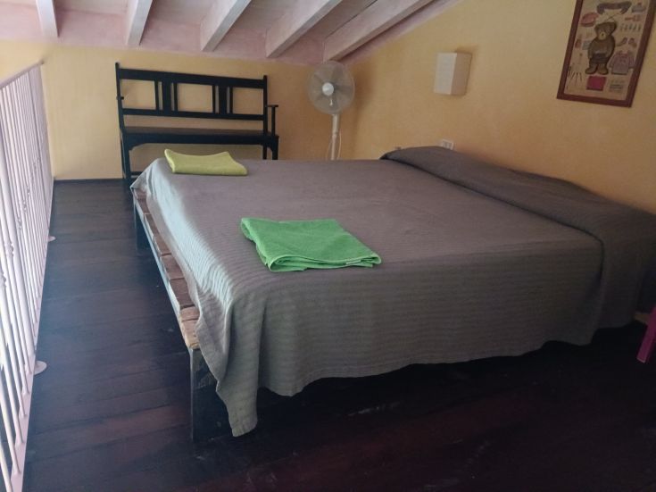 Gemütlicher Raum mit einem großen Bett, lebhaften Bettwäsche und einem Ventilator für ein angenehmes Ambiente.