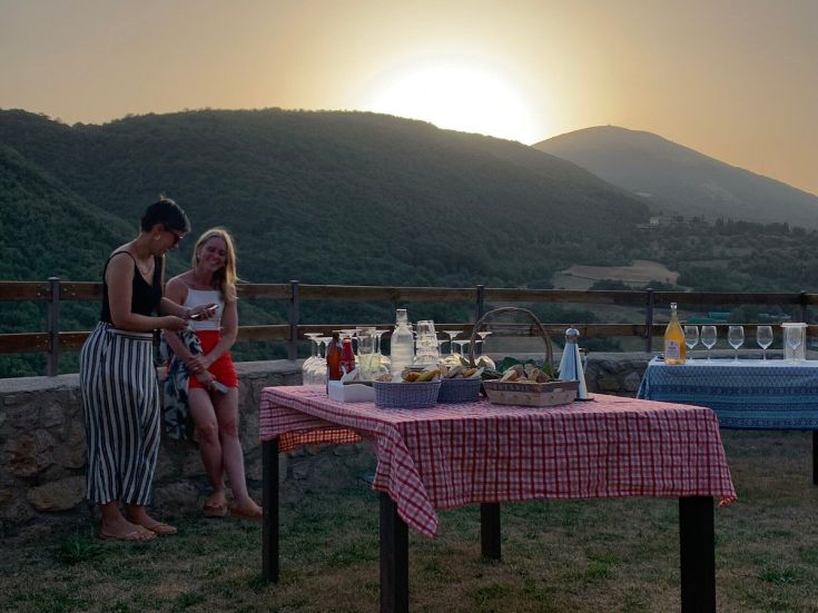 Abend mit Freunden in entspannter Atmosphäre, Tisch mit Essen und Getränken gedeckt, Blick auf die Hügel, die im Sonnenuntergang leuchten.
