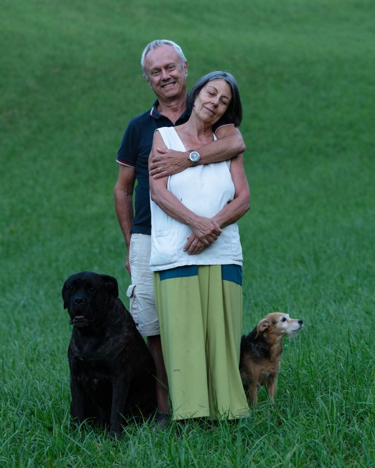 Ein lächelndes Paar auf einem grünen Feld mit ihren Hunden, in einem Moment der Ruhe und Zuneigung.