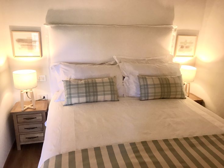 Camera semplice con letti bianchi e tende a righe, illuminata da lampade sobrie.