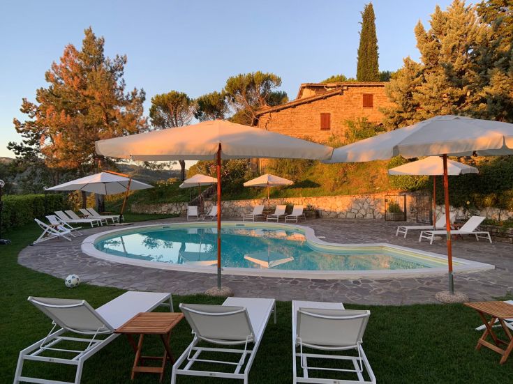 Piscina immersa nel verde, circondata da alberi e ombrelloni, in un ambiente sereno e rilassato.