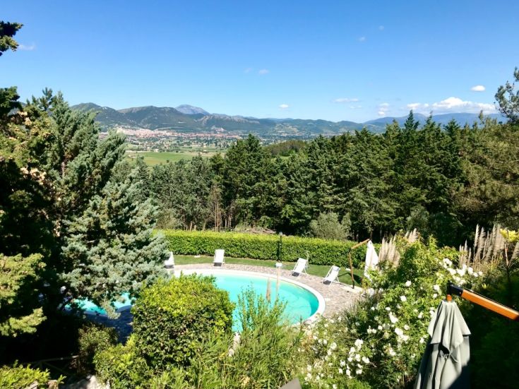 Piscina grande circondata da un giardino curato, panoramica su Gubbio e colline circostanti.