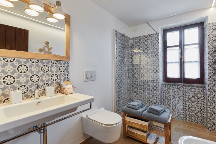 Bagno semplice con piastrelle chiare, doccia in vetro e asciugamani sistemati.