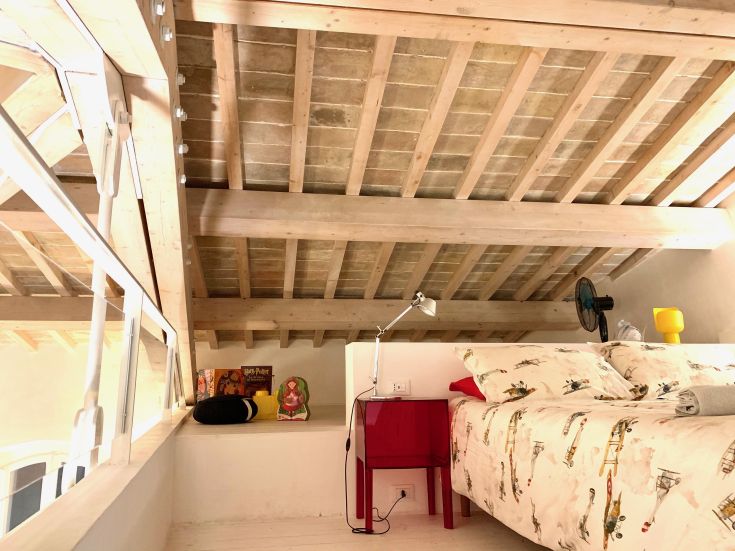Simple room with wooden beam ceiling, basic beds, and a functional reading nook.