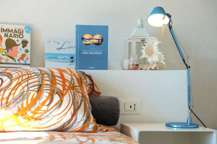 Simple and well-lit bedroom featuring a blue lamp, a patterned pillow, and a small bookshelf.
