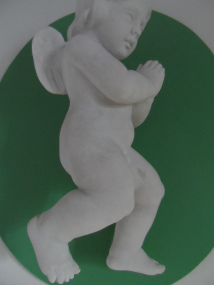Scultura in marmo che raffigura un angelo in posizione infantile, caratterizzata da dettagli semplici e linee morbide.