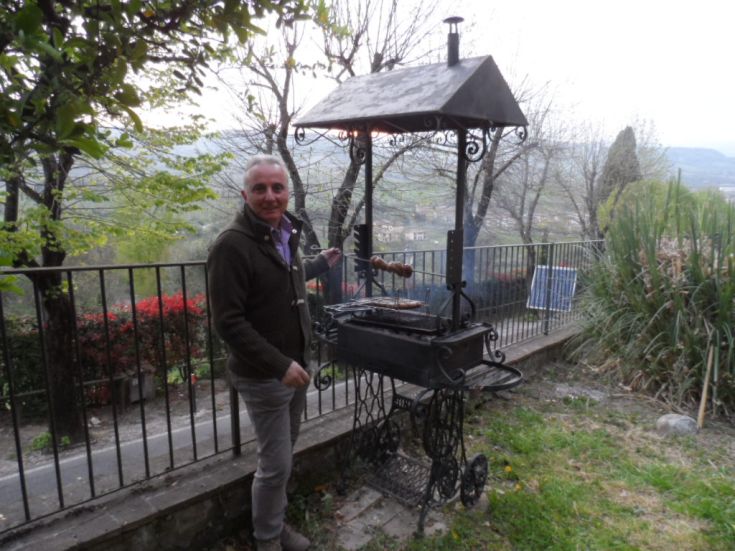 Un uomo sta preparando cibo alla griglia in un tranquillo giardino, circondato da alberi e piante.