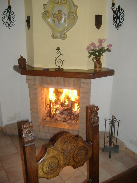 Un camino acceso in un ambiente rustico, con elementi in legno e ferro. Atmosfera calda e familiare.