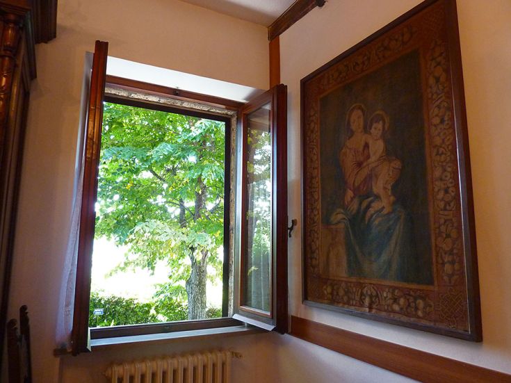 Scena di una finestra aperta che mostra un quadro di una madonna e un curato giardino all'esterno.