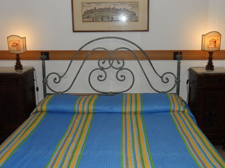 Camera semplice con letto in ferro battuto e decorazioni tradizionali. Atmosfera accogliente e colori armoniosi.