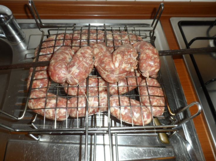 Salsicce artigianali in attesa di cottura su una griglia in metallo, pronte per essere gustate.