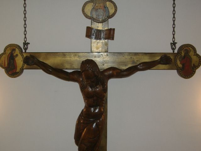 Crocifisso in legno, rappresentato in modo semplice. È visibile sulla parete di una chiesa.
